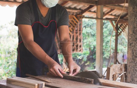Foto de El carpintero asiático está usando una sierra circular para cortar madera para construir una caja de almacenamiento en una mesa de escritorio en su fábrica. Trabajando como su propio jefe en el concepto de casa - Imagen libre de derechos