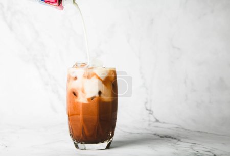 Téléchargez les photos : Verser du lait faire cacao glacé en verre clair sur marbre, espace de copie pour votre tex - en image libre de droit