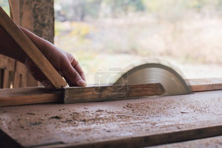 Photo for Asian carpenter is using a circular saw to cut wood to construct a storage box on a desk table at his factory. Working as your own boss at home concept - Royalty Free Image