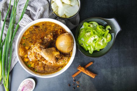 Téléchargez les photos : Des pilons de poulet thaïlandais cuits dans la sauce aux herbes et aux œufs avec du chili, de l'oignon, de l'oignon rouge et une assiette de cannelle sur fond de marbre noir. Copiez l'espace pour votre texte - en image libre de droit