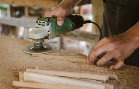 Photo for Asian carpenter is sanding wood using an electric wood sander to smooth the wood surface on a workbench at his factory. Small Business , working as your own boss at home Concept - Royalty Free Image