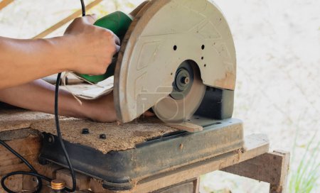 Téléchargez les photos : Le menuisier asiatique utilise une scie circulaire pour couper du bois afin de construire une boîte de rangement sur une table de bureau à son usine. Travailler comme votre propre patron à la maison concept - en image libre de droit