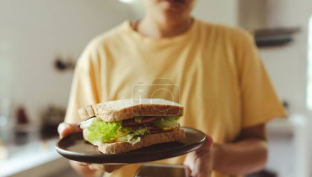 Téléchargez les photos : Les mains tiennent un délicieux sandwich à la saucisse de bologne, une assiette, un œuf frit et de la laitue. - en image libre de droit