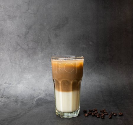 Téléchargez les photos : Café latte est stratifié avec du lait. Boisson à la caféine froide sur un verre transparent et grains de café torréfiés sur fond de marbre noir. studio photo - en image libre de droit