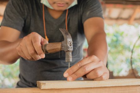 Foto de Artesano de madera usando un martillo clavos martilleo madera hacer que el producto de trabajo en carpintería taller muebles proyecto - Imagen libre de derechos