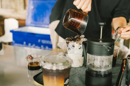 Foto de El camarero prepara, prepara o vierte chocolate en un vaso de leche para poner el cacao helado en la mesa con el equipo para hacer café. Enfoque selectivo y suave - Imagen libre de derechos