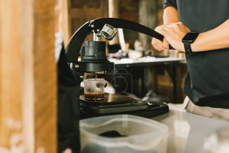 Téléchargez les photos : Un barista utilisant le Flair Espresso Maker est un appareil de brassage de café non électrique utilisant un levier ou une poignée. Pour extraire l'expresso sur une table avec cafetière café glacé. foyer doux - en image libre de droit