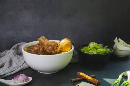 Téléchargez les photos : Des pilons de poulet thaïlandais cuits dans de la sauce aux herbes et des œufs avec du chili, de l'oignon, de l'oignon rouge et une assiette de cannelle sur fond de marbre noir. Copiez l'espace pour votre texte - en image libre de droit