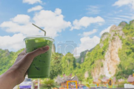 Photo for Hand holding a glass of green tea and cold milk Behind is a view of the mountains and blue sky in background. Leave some space for letters for you. - Royalty Free Image