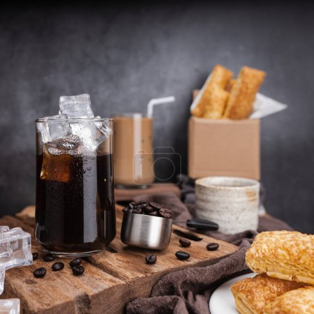 Photo for Iced of americano coffee cup on glass cup with biscuits and roasted coffee beans on the table - Royalty Free Image