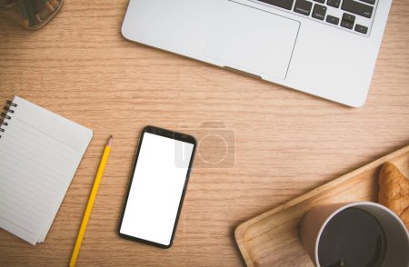 Foto de Vista superior del teléfono inteligente móvil negro blanco maqueta de espacio de copia en blanco para su uso. escritorio con ordenador portátil y croissant café, cuaderno y lápiz en la mesa de madera - Imagen libre de derechos