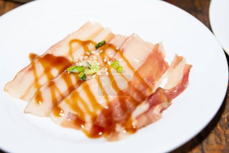 Téléchargez les photos : Ventre de porc émincé et huître de soja garnie d'oignons de printemps Ingrédients et matières premières mangeant du shabu, du sukiyaki et du porc sur une assiette blanche. - en image libre de droit