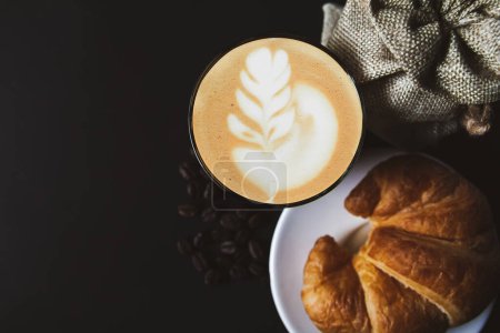 Foto de Café de arte latte en una taza blanca, croissants, café frijol tostado vista superior, fondo negro, copiar el espacio de su texto - Imagen libre de derechos