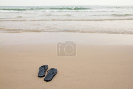 Photo for Black slippers feet at the beach, with a wave of foaming gentle beneath them. - Royalty Free Image
