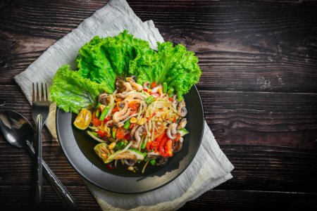 Photo for Papaya salad with squid tentacles, dried shrimp, tomatoes, long beans and peanuts seasoned with fish sauce, sugar, and lime on a plate placed on a wooden board, leaving space for letters. - Royalty Free Image