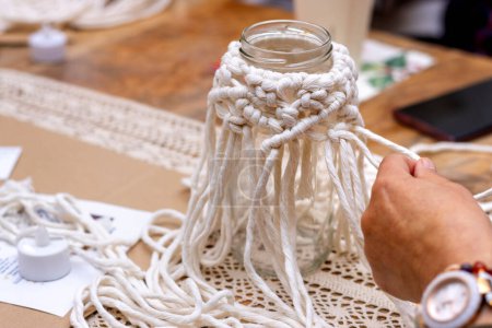 Téléchargez les photos : White macram. Close up of a woman's hands weaving a glass jar with macram. - en image libre de droit
