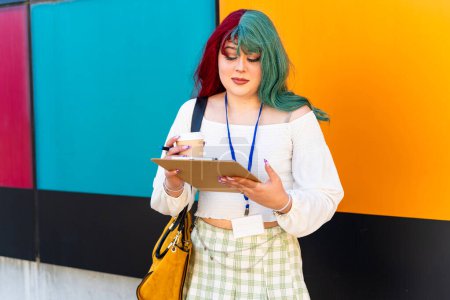 Modernes Mädchen mit rotem und grünem Haar überprüft einige Aufgaben im Notizbuch