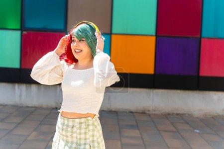 Modern girl with red and green hair putting on green headphones