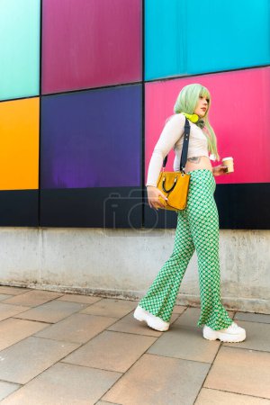 Trendiges Mädchen mit grünen Haaren hält einen Kaffee zum Mitnehmen in der Hand und läuft durch die Kunstschule