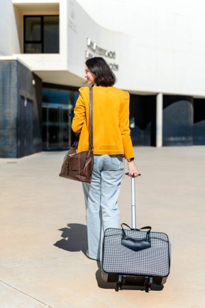 Mujer de negocios rumana caminando hacia una oficina moderna con una maleta