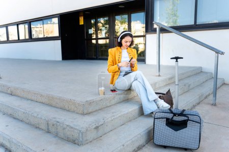 Téléchargez les photos : Femme d'affaires avec écouteurs assis sur les escaliers dans le bureau - en image libre de droit