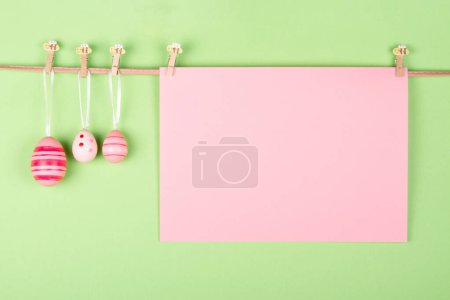 Téléchargez les photos : Feuille de papier pastel rose vierge et trois œufs de Pâques roses accrochés à la corde sur fond pastel vert clair. Idée de carte de vœux de Pâques avec espace vide pour vos mots - en image libre de droit