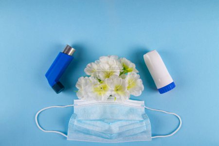 Téléchargez les photos : Deux inhalateurs bleus, masque médical et fleurs blanches sur fond bleu avec un espace négatif pour le placement de la copie. Sensibilité respiratoire asthme Concept - en image libre de droit
