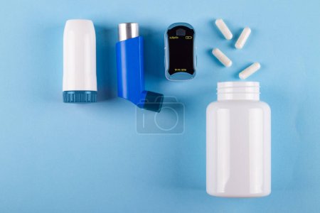 Foto de Vista superior de oxímetro, frasco de pastillas e inhaladores sobre fondo azul con espacio para copiar. Concepto de irritación bronquial causada por el asma - Imagen libre de derechos