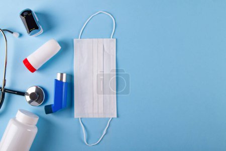 Téléchargez les photos : Vue du dessus du masque médical, stéthoscope, oxymètre, bouteille de pilules et inhalateurs sur fond bleu avec espace de copie. Notion de difficulté à inhaler causée par l'asthme - en image libre de droit