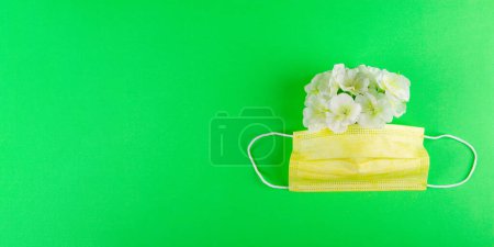 Foto de Máscara médica amarilla y flores blancas sobre fondo verde vibrante con espacio de copia en el lado izquierdo. Enfermedad alérgica de las vías respiratorias Concep - Imagen libre de derechos