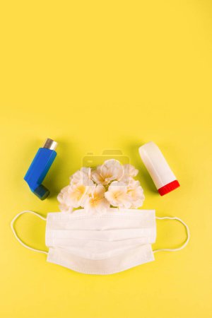 Téléchargez les photos : Inhalateurs, masque médical et fleurs printanières sur fond jaune avec espace vide pour le texte en haut. Concept de difficulté à respirer causée par une allergie - en image libre de droit