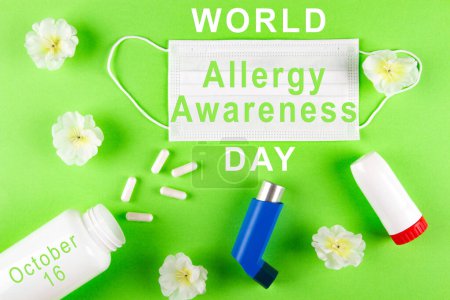Téléchargez les photos : Journée mondiale de sensibilisation aux allergies célébrée le 16 octobre. Affiche avec inscription blanche, masque chirurgical, fleurs, inhalateurs et bouteille avec des pilules sur fond vert clair vibrant - en image libre de droit