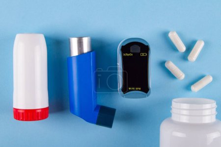 Téléchargez les photos : Vue du dessus de l'oxymètre, bouteille de pilules et inhalateurs sur fond bleu avec. Concept de sensation thoracique serrée causée par l'asthme - en image libre de droit