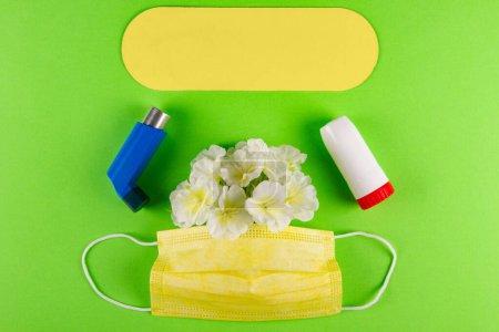 Téléchargez les photos : Inhalateurs, masque jaune et fleurs blanches sur fond vert clair avec plaque jaune pour inscription. Concept de difficulté à respirer profondément causée par l'asthme - en image libre de droit