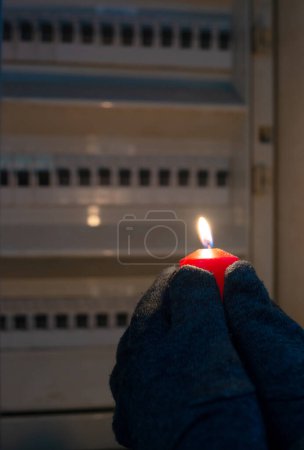 Photo for Blackout, standing with a candle in front of a power fuse box, energy cut out, uncertain supply, risk and crisis for electricity - Royalty Free Image