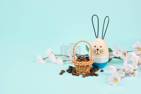 Photo for Wicker basket with roasted coffee beans, an easter bunny and cherry blossom, greeting card holiday, spring season - Royalty Free Image