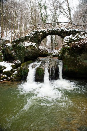 Foto de Scheissendempel waterfall, river Black Ernz with stone bridge covered with snow, Mullerthal trail in Waldbillig, Luxembourg in winter - Imagen libre de derechos