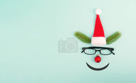 Téléchargez les photos : Face of a reindeer with a red bauble nose, fir antlers, a santa claus hat and eyeglasses, merry christmas greeting card - en image libre de droit