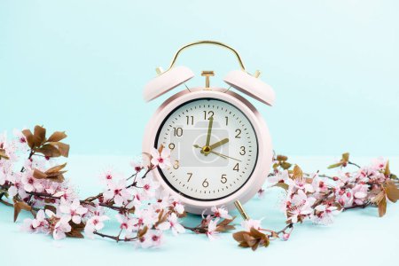 Foto de Reloj despertador con flores de cerezo, cambio a horario de verano en primavera, cambio de horario de verano - Imagen libre de derechos