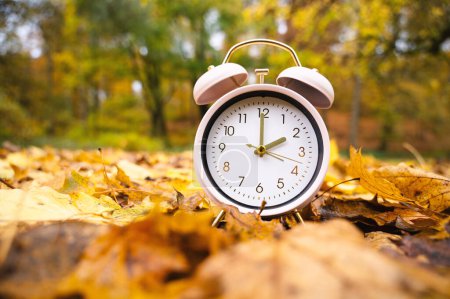 Alarm clock with autumn foliage, end of daylight saving time in fall, winter time changeover