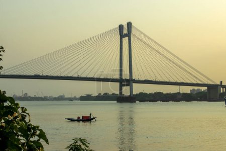 Photo for Boat in the river Ganges at Kolkata. It is a toll bridge over the Hooghly River in West Bengal, India, linking the cities of Kolkata and Howrah. - Royalty Free Image