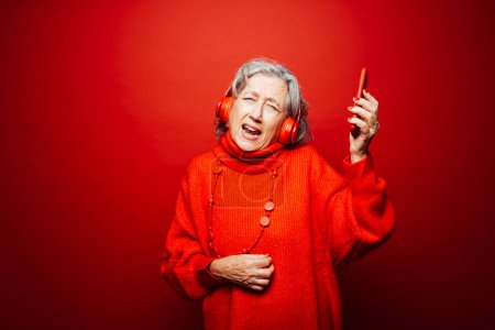 Photo for Senior woman wearing red clothes, with red headphones and red smartphone, dancing over a red background - Royalty Free Image