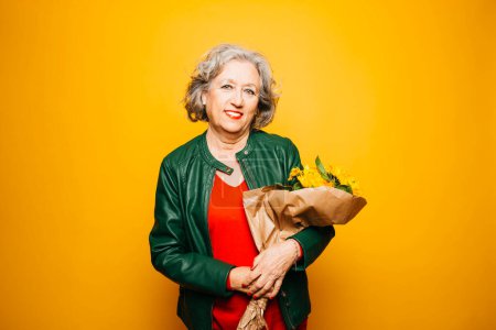 Photo for Portrait of a senior woman applying red lipstick over a yellow background - Royalty Free Image