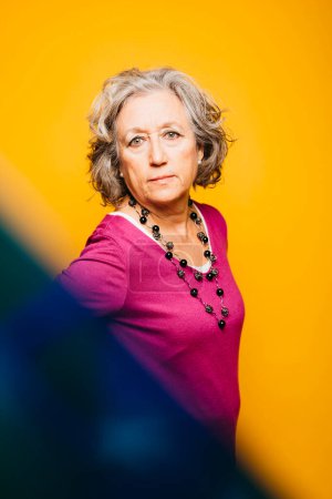 Photo for Portrait of a senior woman wearing pink sweater over a yellow background - Royalty Free Image