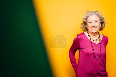 Photo for Portrait of a senior woman applying red lipstick over a yellow background - Royalty Free Image