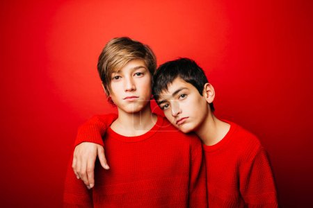 Photo for Two Pre-adolescent boys, wearing a red sweater, embracing over a red background - Royalty Free Image