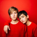 Two Pre-adolescent boys, wearing a red sweater, embracing over a red background