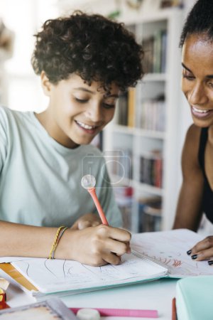 Foto de Mujer alegre ayudando a su hija a hacer la tarea. Madre feliz ayudando a su hija con el trabajo escolar en la sala de estar. - Imagen libre de derechos