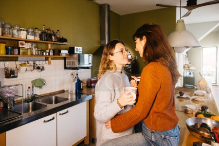 Junges weibliches Paar bei einer Tasse Tee in der heimischen Küche. Lesbisches Paar genießt einen Moment zusammen, nippt an Tee in der heimischen Küche.
