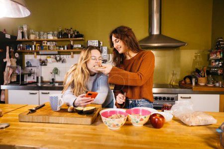A lesbian couple preparing breakfast and sharing a toast, in the cozy atmosphere of their kitchen at home.